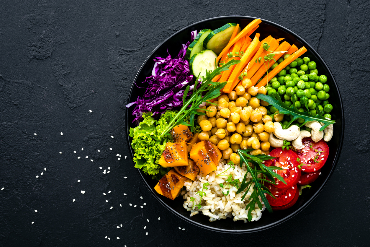 Plant-based diet for beginners: Bowl dish with grains, cucumber, tomato, green peas, red cabbage, chickpea, fresh lettuce salad and cashew nuts.