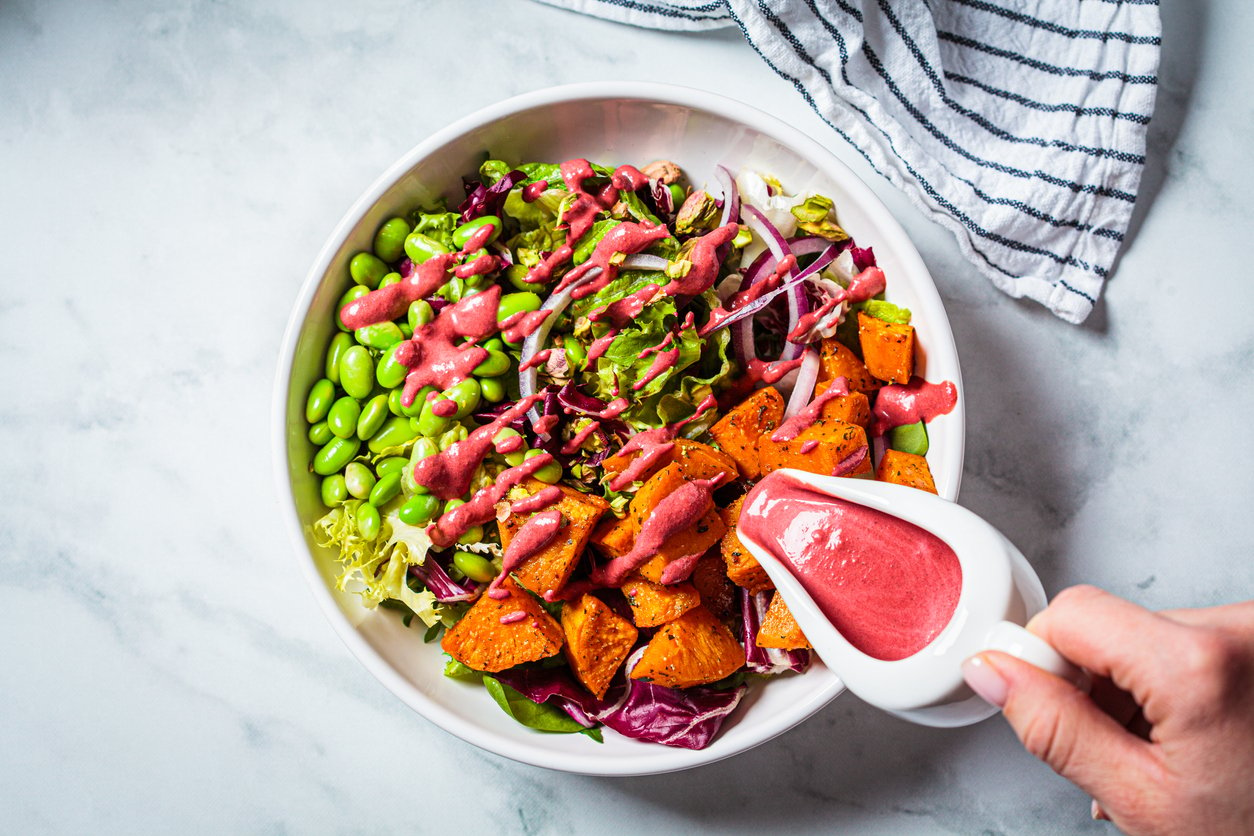 Vegan salad bowl with baked sweet potato, edamame beans, nuts and pink beetroot dressing. Vegan food concept.