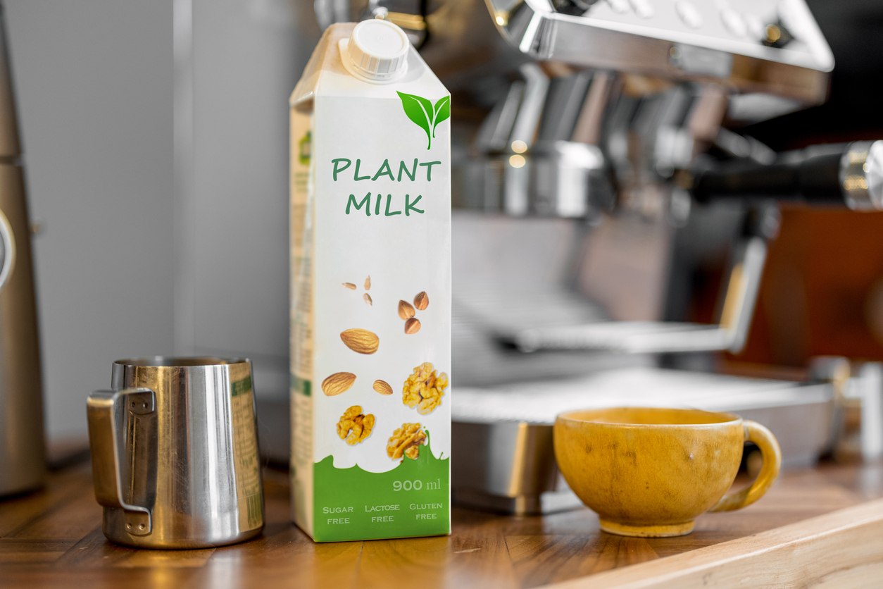 Packaging of vegetable milk near a cup of coffee