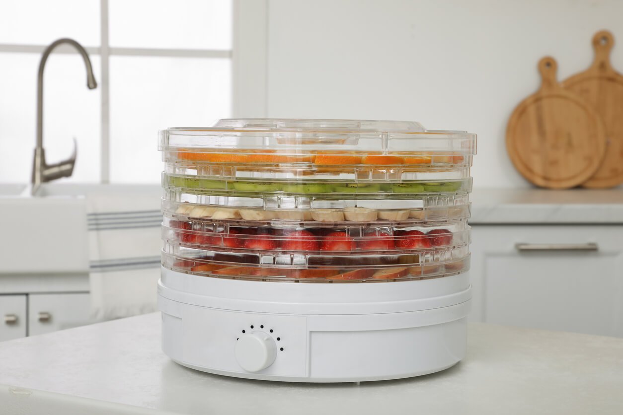 dehydrator machine with different fruits and berries on white table in kitchen