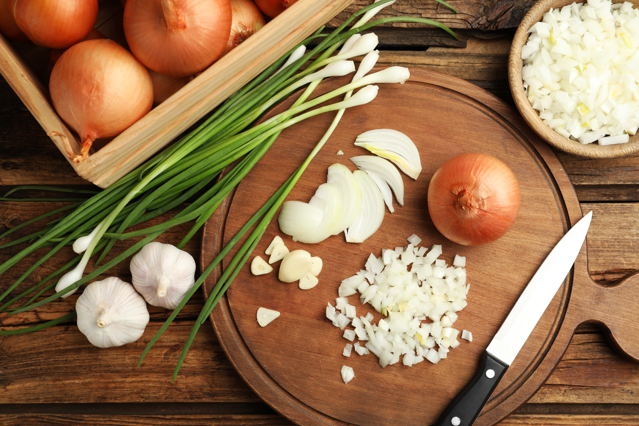 Board with cut onion and garlic on wooden table, flat lay