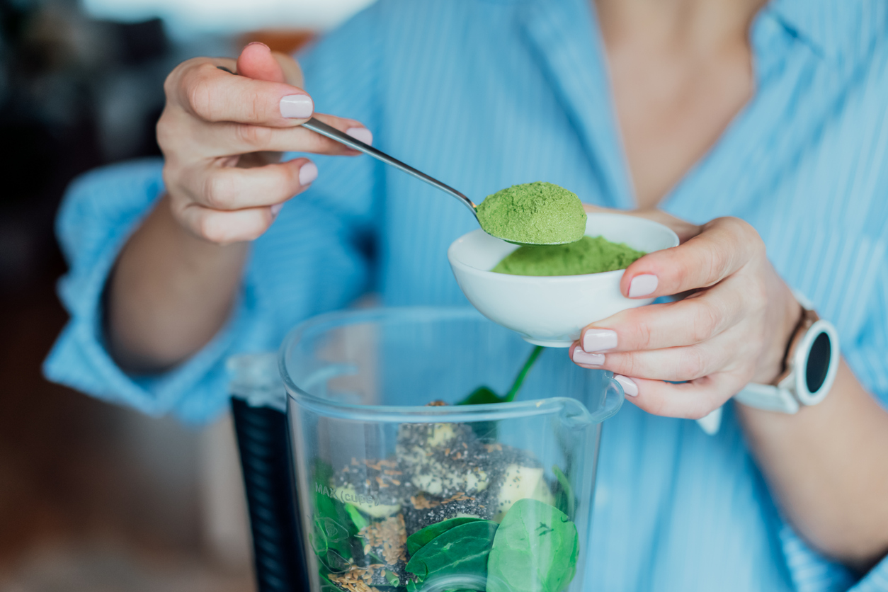 Close up woman adding wheat grass green powder during making smoothie on the kitchen. Superfood supplement. Healthy detox vegan diet. Healthy dieting eating, weight loss program. Selective focus