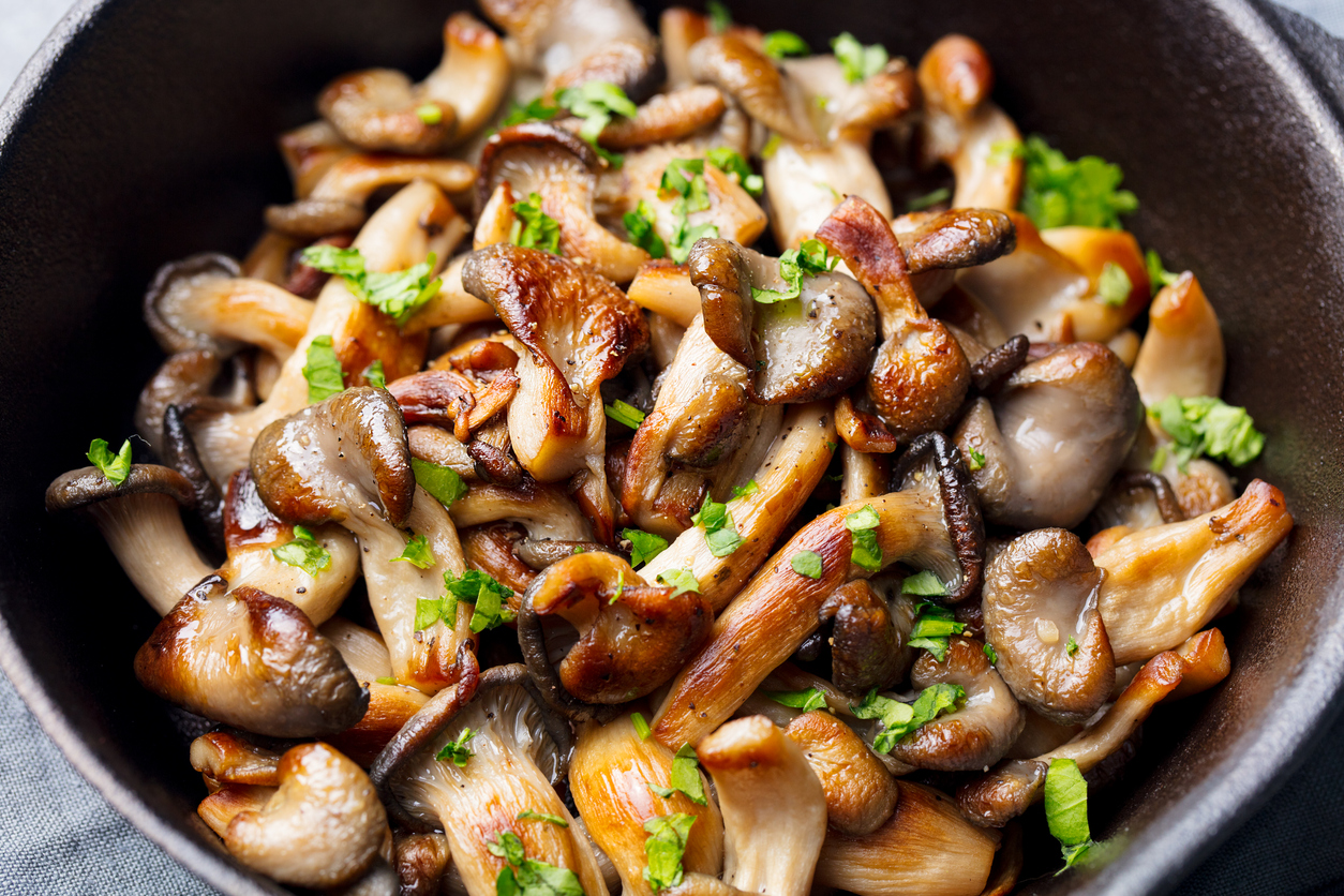 Fried mushrooms with fresh herbs in black cast iron pan.